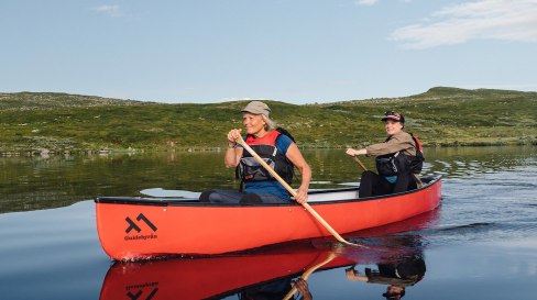 Två personer paddlar kanot i fjällandskap