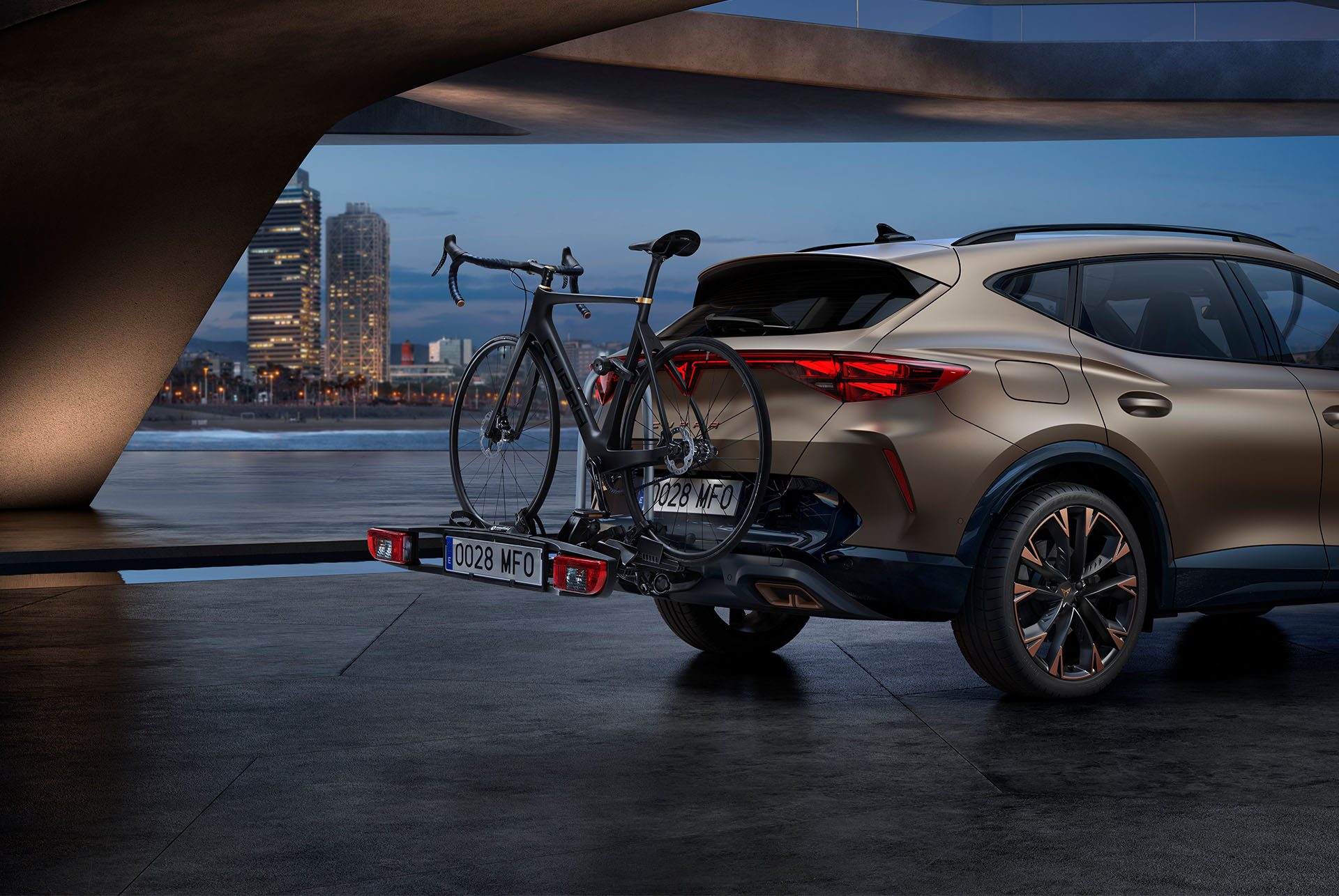 Nya CUPRA Formentor 2024 i sekelbrons med cykelhållare bak och dragkrok, stadens skyline i bakgrunden.