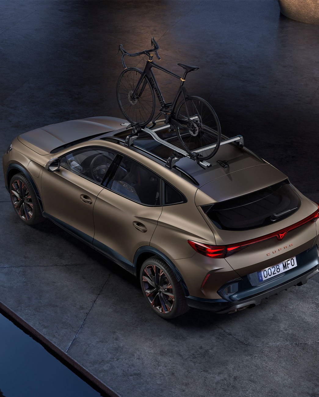 Fågelperspektiv på nya CUPRA Formentor 2024 i matt brons från århundradet med cykelhållare, bil parkerad på betong i skymningen.