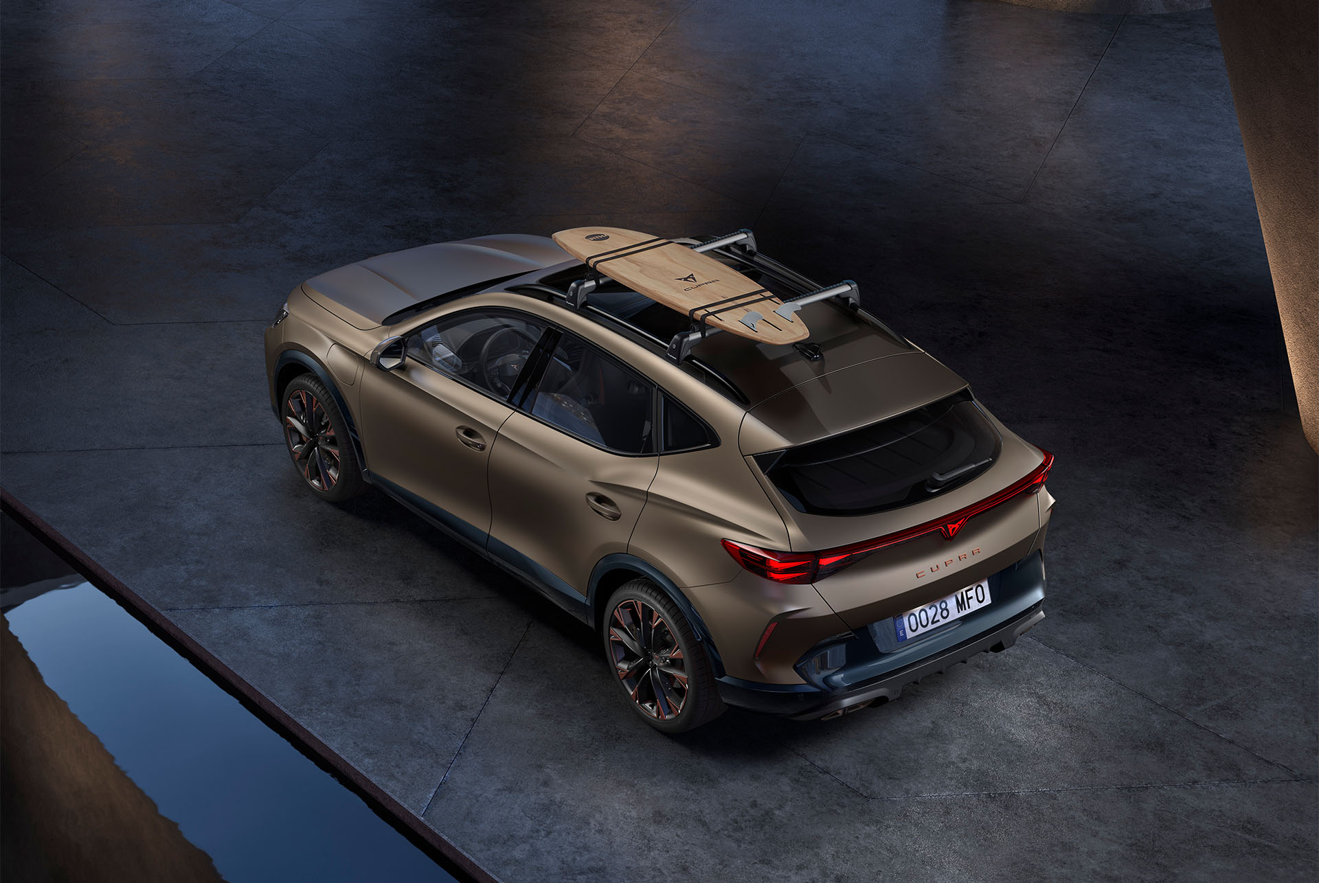 Fågelperspektiv på nya CUPRA Formentor 2024 i matt brons från århundradet med surfbrädshållare på taket, bil parkerad på betong.