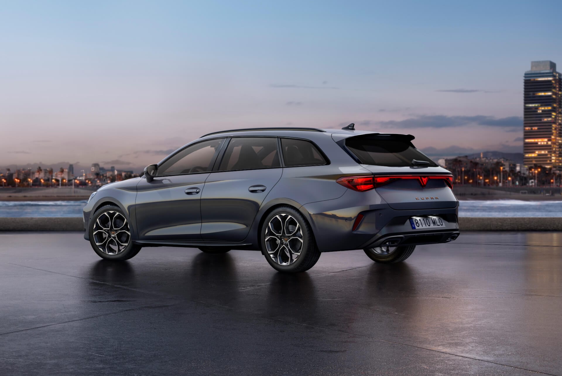 Bild bakifrån av nya cupra leon sportstourer 2024, blankgrå bilmodell med dynamisk chassikontroll samt svarta och kopparfärgade lättmetallfälgar. Stad i bakgrunden vid solnedgång.