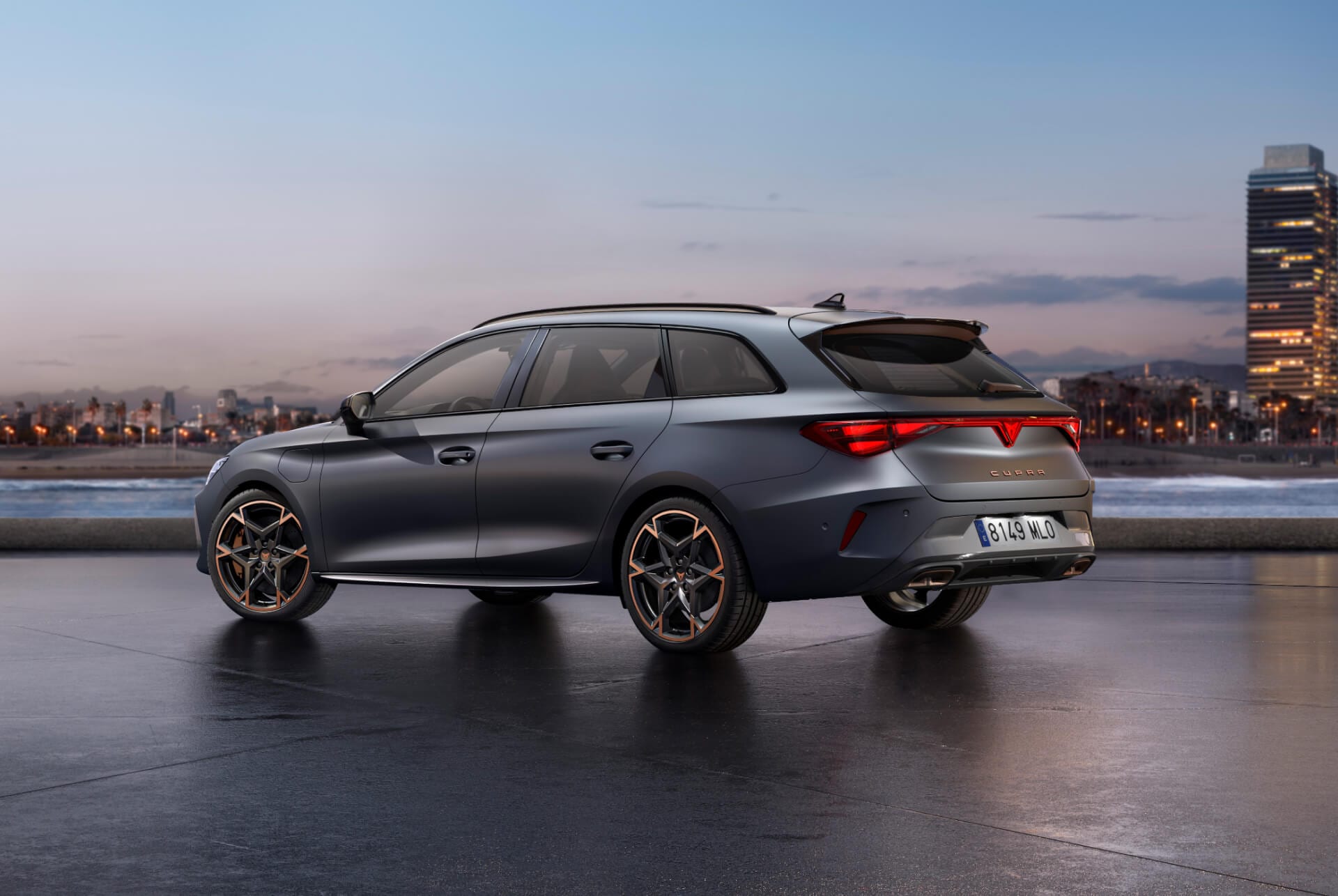Den sportiga nya 2024 Cupra Leon Sportstourer parkerad på betong med en stadssilhuett upplyst i skymningen i bakgrunden. Bilden visar bilen i mattgrå lack.
