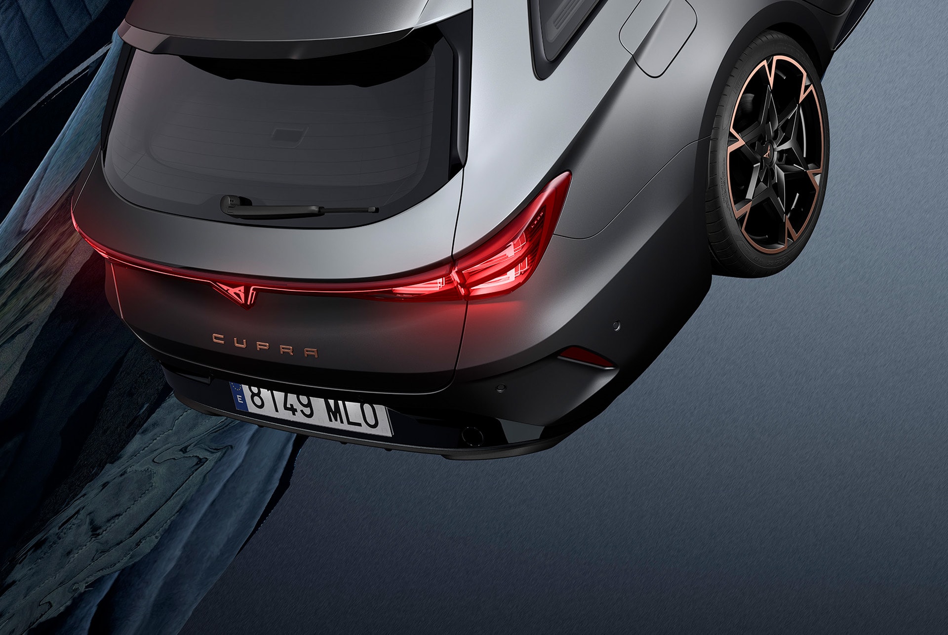 Nya cupra leon sportstourer 2024-bilar och utrustning parkerade på cement, struktur med glödande kanter, med utsikt över stadens skyline i skymningen. Bilen visas i matt grå lack med kopparfärgade och svarta lättmetallfälgar.