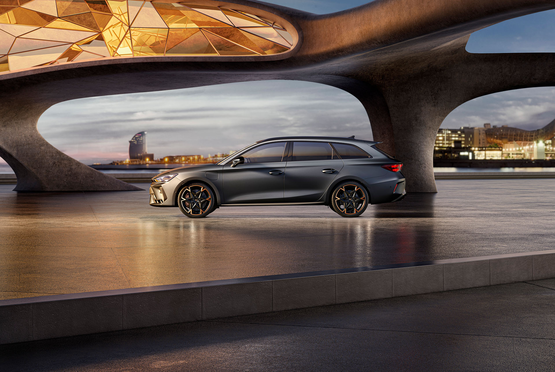 Nya cupra leon sportstourer 2024-bilar och utrustning parkerade på cement, struktur med glödande kanter, med utsikt över stadens skyline i skymningen. Bilen visas i matt grå lack med kopparfärgade och svarta lättmetallfälgar.