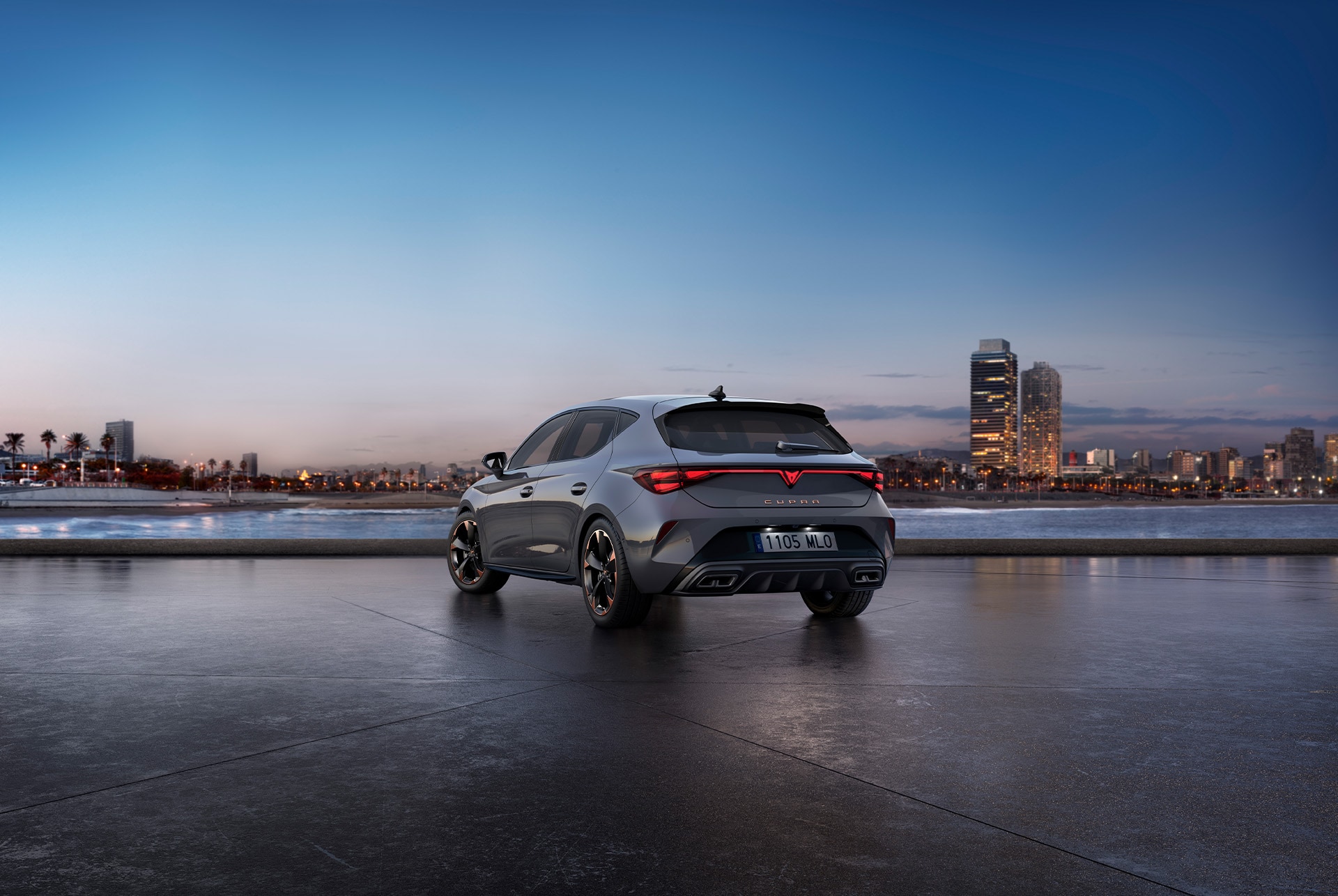 Bild bakifrån av den nya blankgrå bilmodellen cupra leon 2024 med dynamisk chassikontroll samt svarta och kopparfärgade lättmetallfälgar. Stad i bakgrunden vid solnedgång.