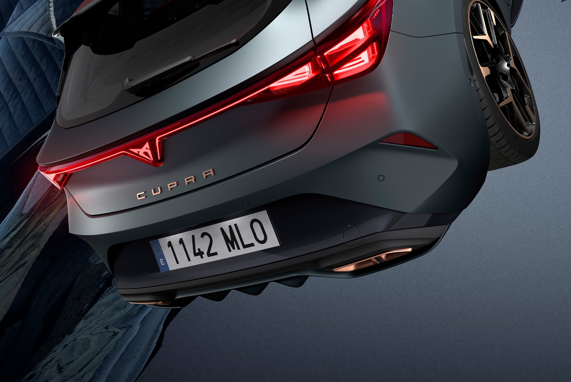 Cupra Leon laddhybridbilsteknik, LED-bakljus, phev-fordon parkerat på cement, struktur med glödande kanter. Bilen visas i matt grå lack med smidda kopparfälgar och svarta fälgar
